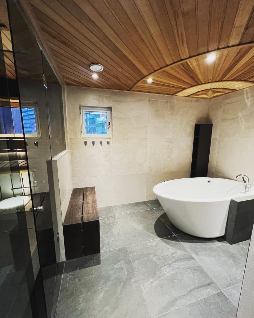 Kylpyhuone vapaasti seisovalla ammeella ja kaarevalla puukatolla
