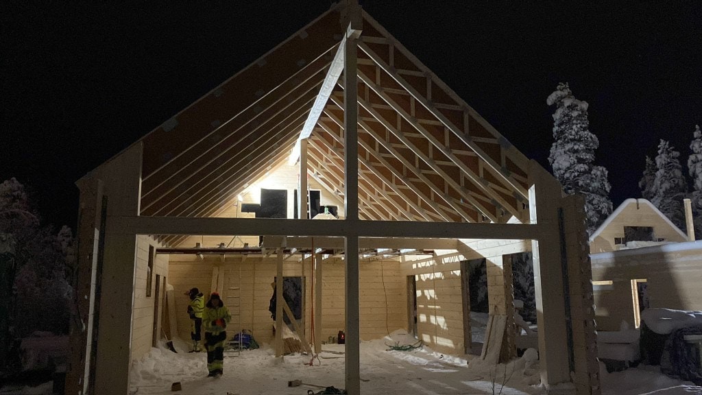 Hirsirunkoinen talo rakenteilla illalla, työmaa valaistuna lumisessa metsässä